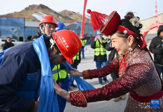 12月30日，在位于新疆和静县的天山胜利隧道出口，和静县乌兰牧骑队演员（右）向施工方代表敬献哈达。新华社记者 胡虎虎 摄